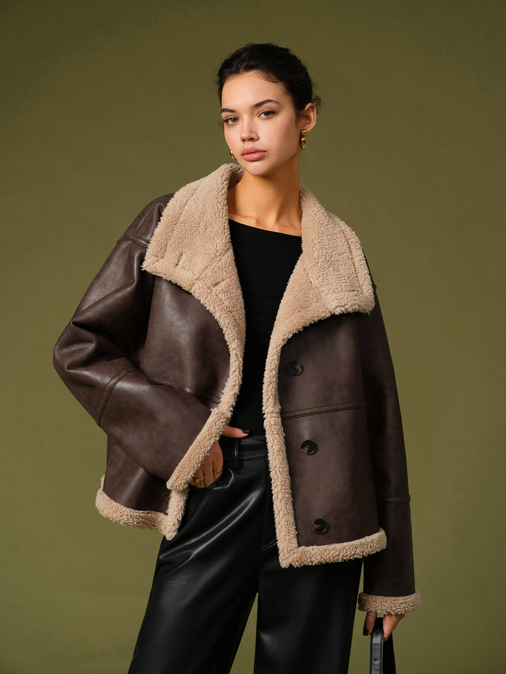 Woman wearing a brown leather jacket with beige fur lining against a green background