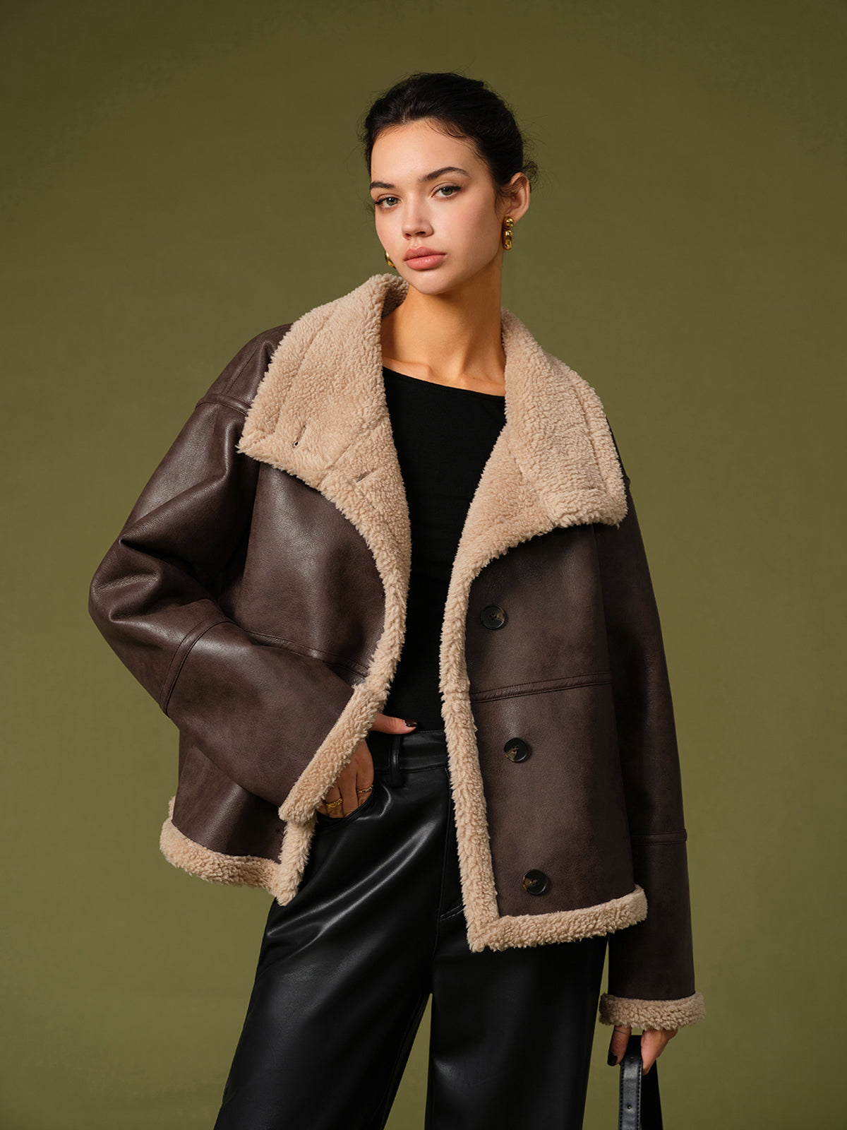 Woman wearing a brown leather jacket with beige fur lining against a green background