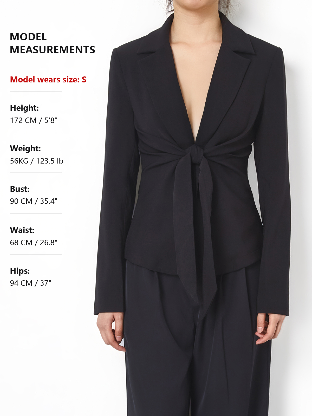 A model wears a black wrap-style blazer with a front tie detail and matching dark trousers against a plain light background. Text on the left lists model measurements including height, weight, bust, waist, and hips.